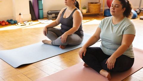 Plus-size women practicing mindful meditation on mats in sunlit yoga studio