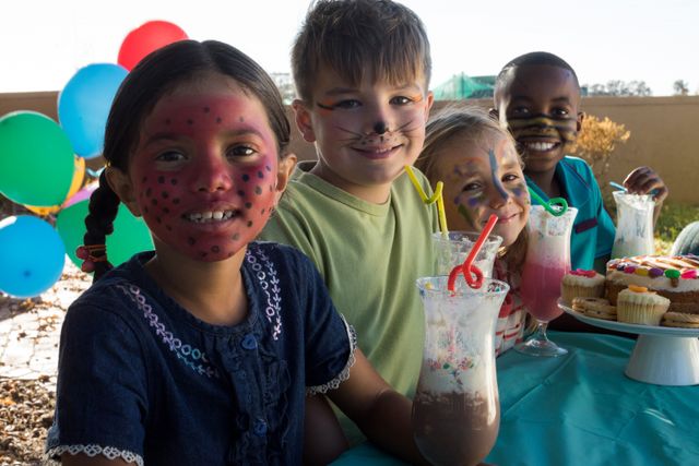 Portrait of smiling children with face paint sitting by food and drinks at park