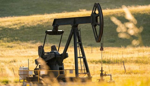 Black pumpjack pumping crude in sunlit rural field during golden hour energy scene