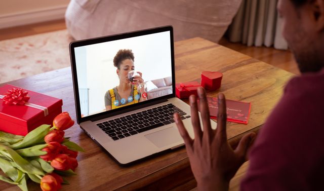 This image showcases a couple celebrating Valentine's Day online, with the woman enjoying red wine while her boyfriend waves during a video call. Perfect for illustrating themes of long-distance relationships, virtual celebrations, and the use of technology to connect loved ones. Ideal for blogs, articles, advertisements, and social media posts about remote communication, romantic online interactions, and special occasions celebrated from afar.