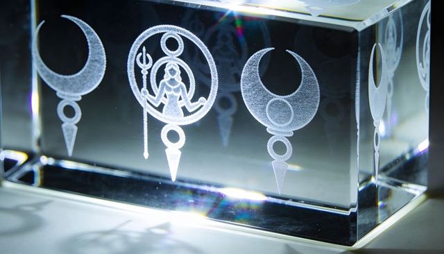 Crystal prism block with etched lunar symbols and goddess figure refracting rainbow light