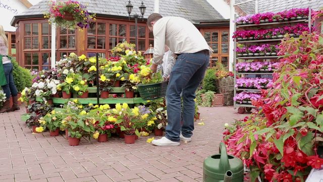 A man with a child is selecting vibrant flowers at a garden center, embodying a family bonding experience and a love for gardening. This scene is perfect for use in advertisements for garden centers, family activities, or parent-child bonding visuals. It conveys themes of nature, togetherness, and weekend leisure activities.