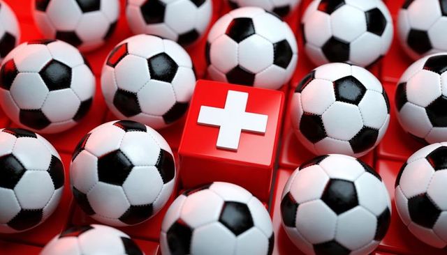 Red swiss cross cube contrasting with black and white soccer balls on glossy red grid
