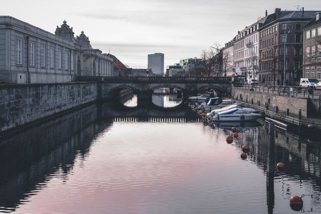 Tranquil urban canal lined with historic European buildings and moored boats during sunset. Reflection of the architecture and soft colors creates a serene atmosphere. Ideal for travel blogs, tourism campaigns, architecture articles, or as a decorative piece showcasing European city charm.