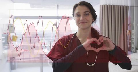 Nurse forming heart with hands wearing maroon scrubs and stethoscope, health data overlay