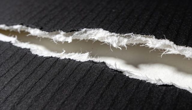 Torn black ribbed paper revealing white fibrous core macro texture and contrast