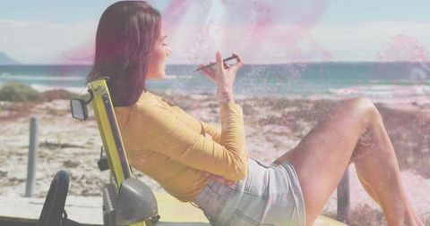 Young woman relaxing on yellow dune buggy at sunny ocean beach holding pen and journaling