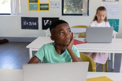 Classroom daydreaming african american boy at laptop, classmate using laptop in background