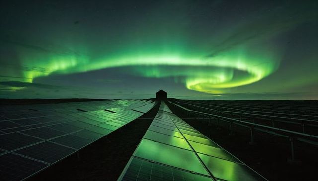 Northern lights reflecting on solar farm panels leading to remote utility hut