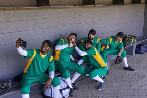 Multicultural baseball team taking dugout selfie wearing green and yellow uniforms