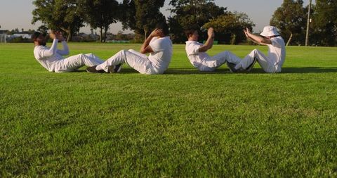 Multicultural cricket teammates doing core exercises on green training field teamwork