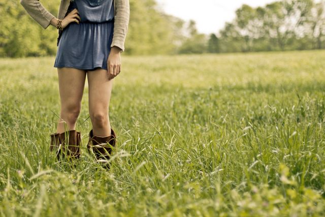 A person wearing casual summer clothing and brown boots standing in tall grass. Ideal for fashion, lifestyle, or nature-themed projects.