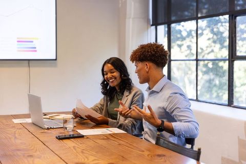African American woman and Hispanic man collaborating over charts and laptop in office