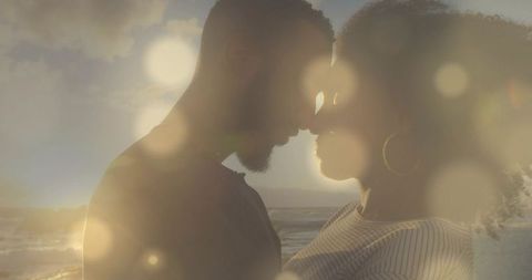 Backlit couple embracing on sunset beach, leaning foreheads, dreamy bokeh ocean silhouette