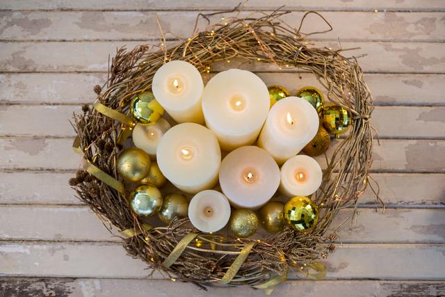 Christmas candles and golden baubles arranged in a rustic wreath on a wooden plank. Ideal for holiday greeting cards, festive home decor inspiration, and seasonal marketing materials.