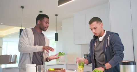 Young men preparing healthy green smoothie together in modern bright open-plan kitchen