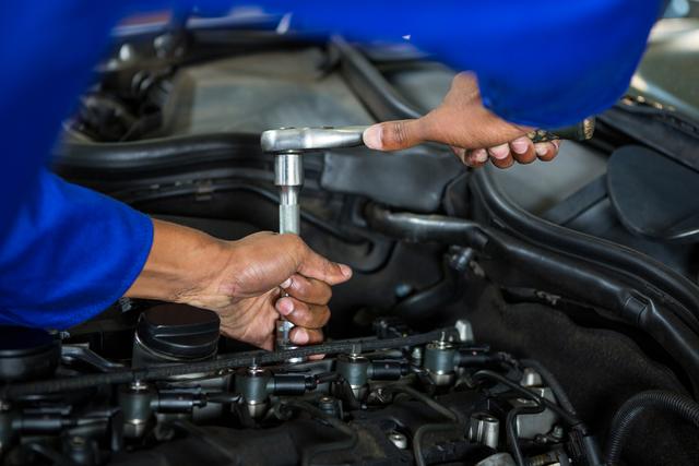 Mechanic using wrench to repair car engine in a garage. Ideal for illustrating auto service centers, mechanical work, vehicle repair services, and automotive maintenance. Great for blogs or articles about car care, mechanical engineering, or technician training programs.