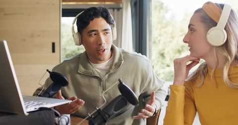 Diverse podcast duo recording lively conversation with microphones and laptop