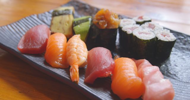 A variety of sushi pieces are presented on a black plate. Sushi is a popular Japanese dish featuring rice with seafood or vegetables.
