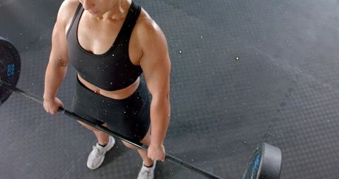 Female athlete gripping barbell during deadlift on rubber gym mat sweating and focused