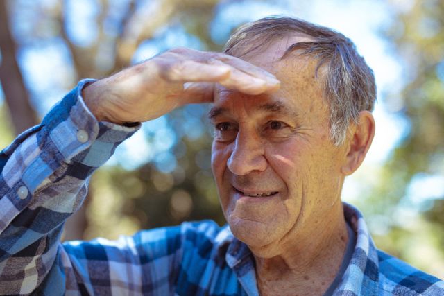Senior man standing in garden, shielding eyes with hand while looking into distance. Ideal for use in articles or advertisements related to retirement, healthy aging, outdoor activities for seniors, and active lifestyles. Can also be used in healthcare and wellness promotions targeting older adults.