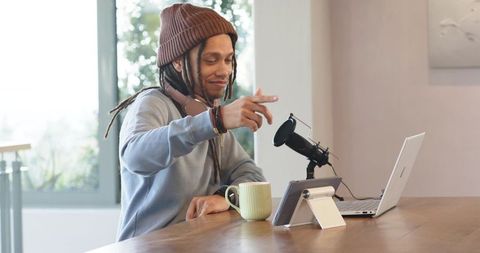African american podcaster recording cozy home studio with laptop, microphone and tablet