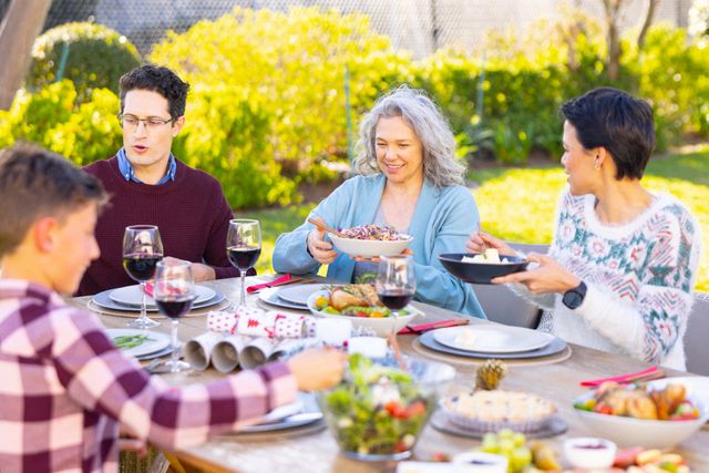 Happy caucasian parents and son eating meal at table in garden with grandmother, copy space. Family, togetherness, domestic life and happiness concept.