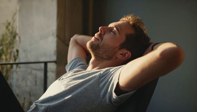 Reclining young man basking in balcony sunlight for calm, relaxation and mindful living