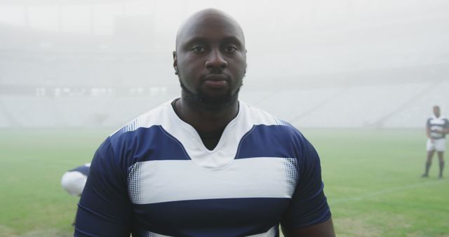 Portrait of bald african american male rugby player in team strip on pitch at misty sports stadium. Rugby, sport, sportsman, confidence and competition, unaltered.