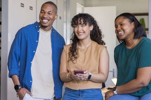 Diverse coworkers laughing and sharing smartphone in modern casual office team collaboration