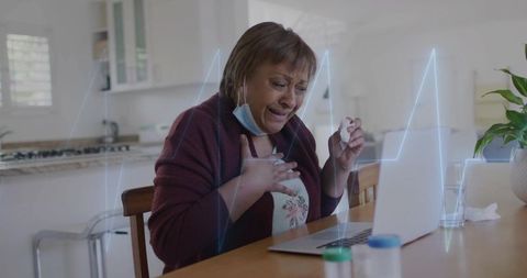 Middle-aged woman experiencing chest pain during telehealth call with laptop and medication