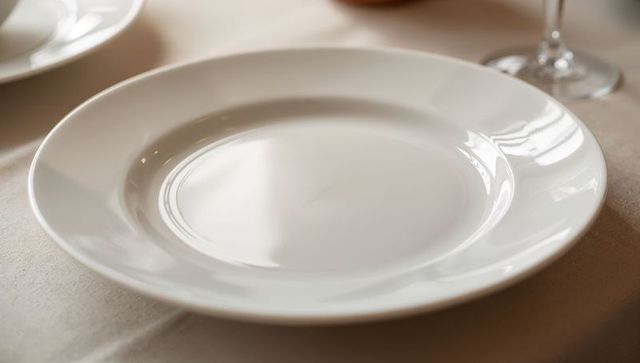 Minimal white porcelain dinner plate on neutral tablecloth with glass stem