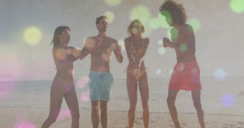 Friends dancing and splashing on sunlit beach with bokeh flare and vintage film grain