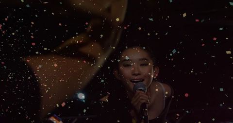 Energetic Female Vocalist Singing on Stage with Vibrant Confetti