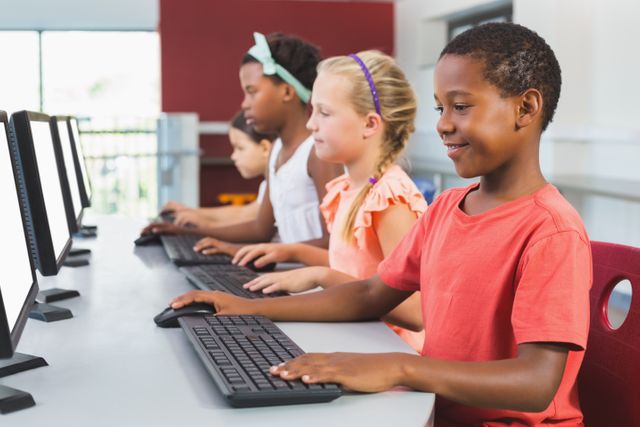 Children of different ethnicities are using computers in a classroom, focusing on their screens. This image can be used for educational content, technology in education, diversity in schools, and teamwork among young students.