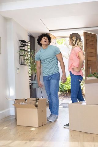 Diverse couple unpacking boxes in sunlit entryway of new home on moving day