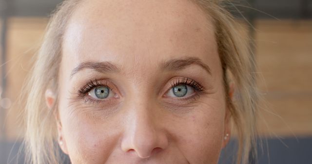 Close-up portrait of a woman with striking blue eyes and natural makeup. Blonde hair frames her face, and her expression is neutral, giving the image a sense of realism and human detail. This can be used for highlighting eye beauty, skincare products, natural look themes, or human-centric content in blogs and advertisements.