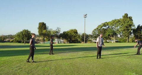 Multicultural friends playing cricket on sunny park field practicing batting and bowling