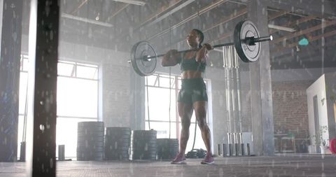 Athletic woman lifting loaded barbell in warehouse gym, displaying strength and focus