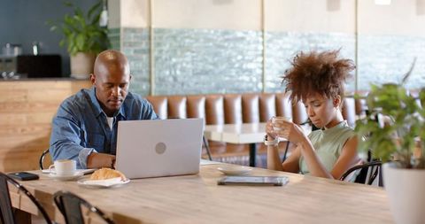 Remote work cafe scene showing focused adults using laptop and smartphone over coffee