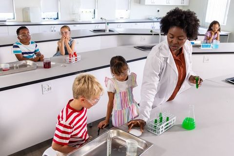 African american teacher leading elementary science experiment with children in modern lab