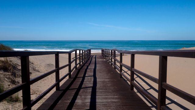 Wooden boardwalk leading to sandy beach and clear blue sea - Download Free Stock Photos Pikwizard.com
