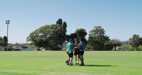 Group of athletes huddling on sunny grassy field celebrating team unity and camaraderie