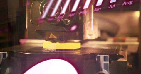 Closeup 3d printer nozzle printing yellow part on heated bed with magenta reflections