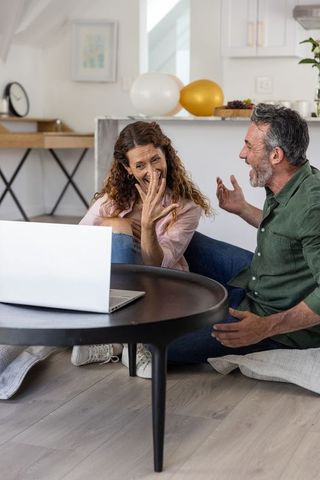 Middle-aged couple celebrating engagement at home showing ring during video call