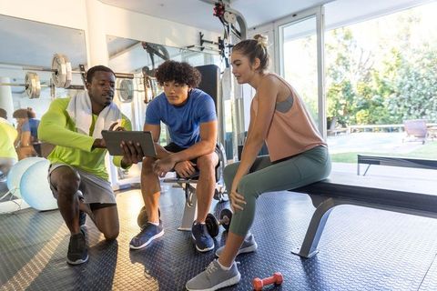Fitness coach guiding two clients with tablet during strength training in bright gym