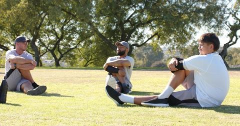 Three men stretching on sunny park lawn during group fitness session and teamwork