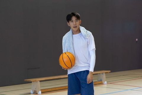 Young asian basketball player holding ball and towel resting on indoor gym court