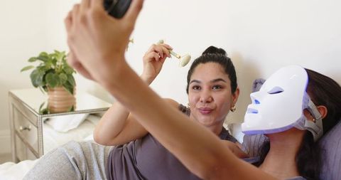 Diverse friends sharing at-home skincare session with led face mask and jade roller