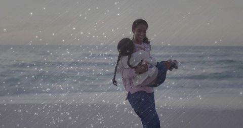 Mother twirling daughter by ocean at dusk with sparkle overlay